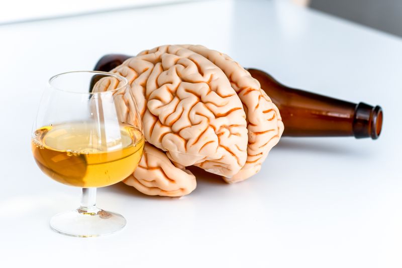 A plastic or rubber brain sitting next to a glass of wine and an upturned beer botle 