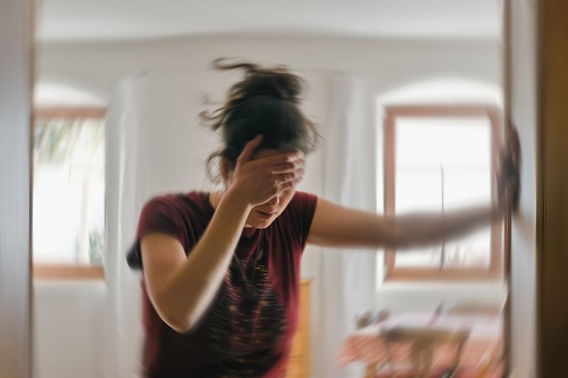 woman covering eyes and leaning on doorframe, with backdrop blurred to indicate dizziness