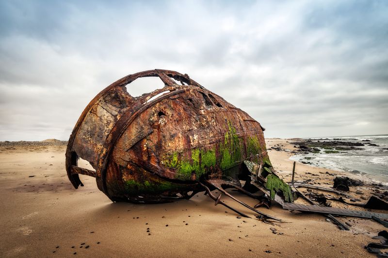 Ship Wreck along the Skeleton Coast in Western Namibia taken in January 2018; carcass of a ship with green bilge on the bottom lying on its side on a beach