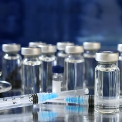 vaccine vials on a table with two syringes in the foreground and a stethoscope 