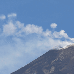 On the right hand side is the top of Mount Etna and the rest of the image is blue sky and white vapor. Above the white vapor are perfect smoke-like rings.